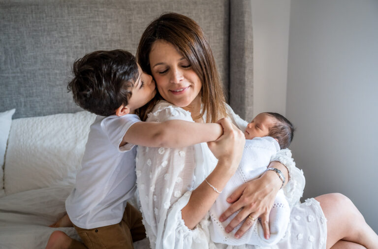 Boy leans in to kiss his mom while she holds a newborn baby