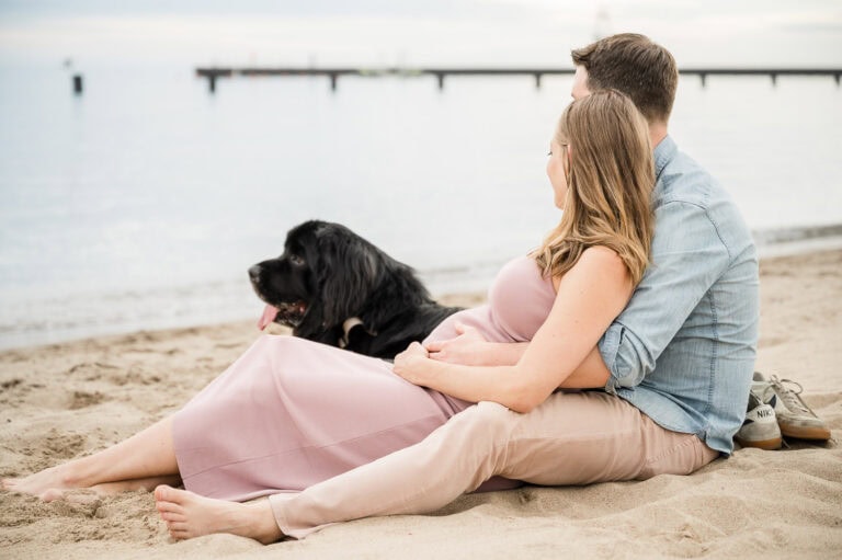 Expectant couple relax on beach with dog