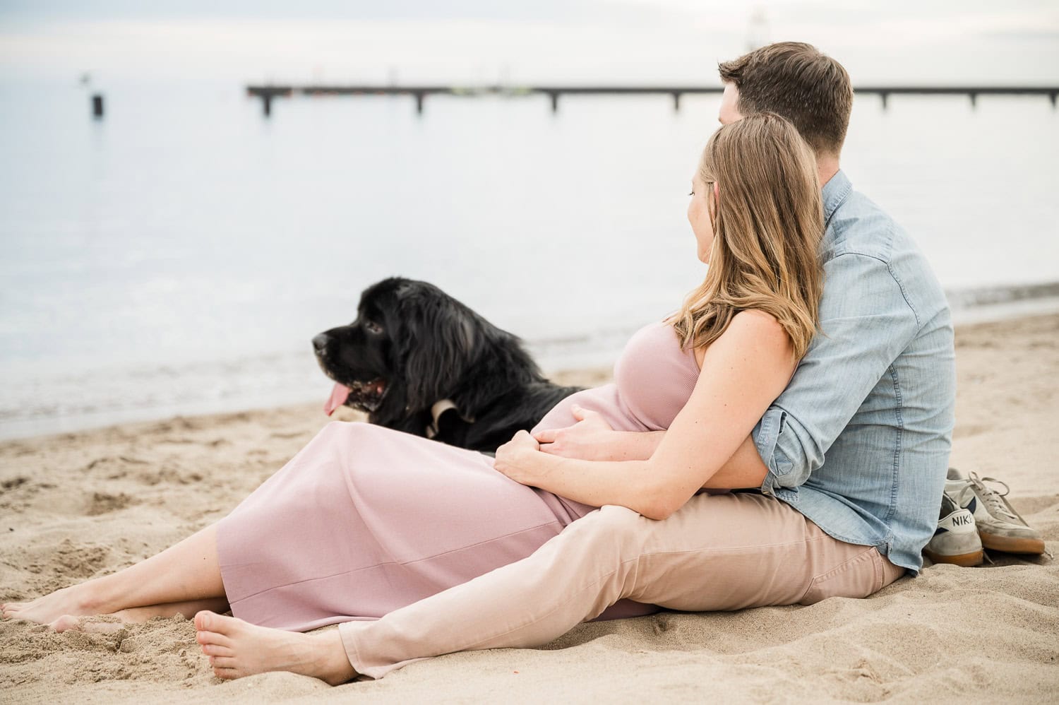 Expectant couple relax on beach with dog