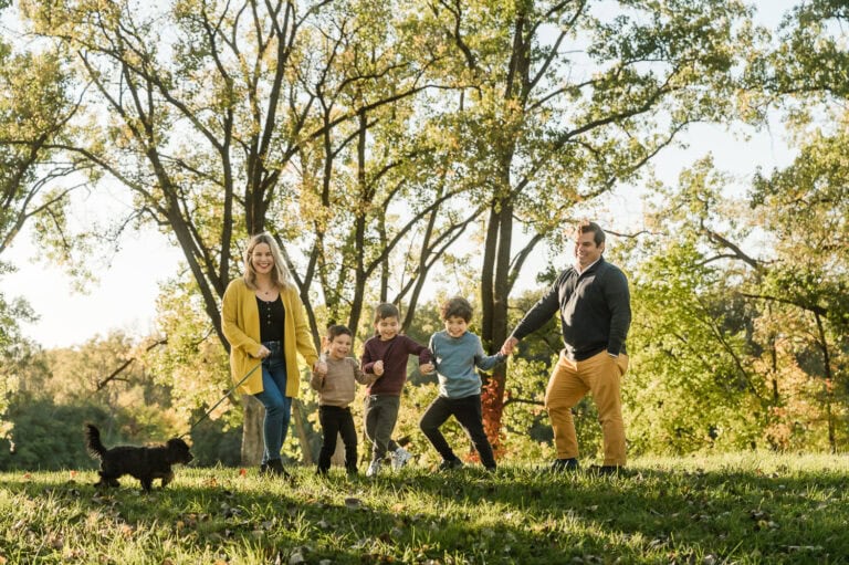 Family with three boys and a dog (un)pose by holding hands in a line and moving around together during a family photo session with Maija Martin Photography