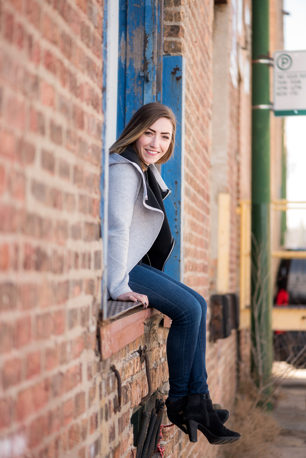 woman sitting on loading dock peers out from the side towards camera with view of alley in Chicago behind her