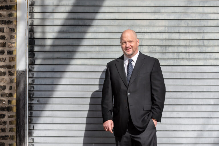 Man in suit leans on gray textured metal background