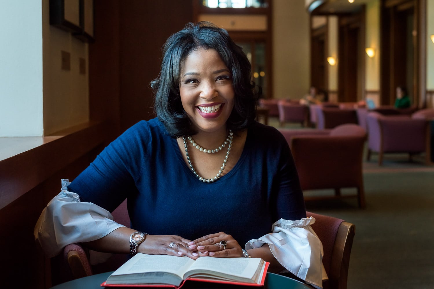 Environmental portrait of a woman who works in education consulting smiles up from open book in university library