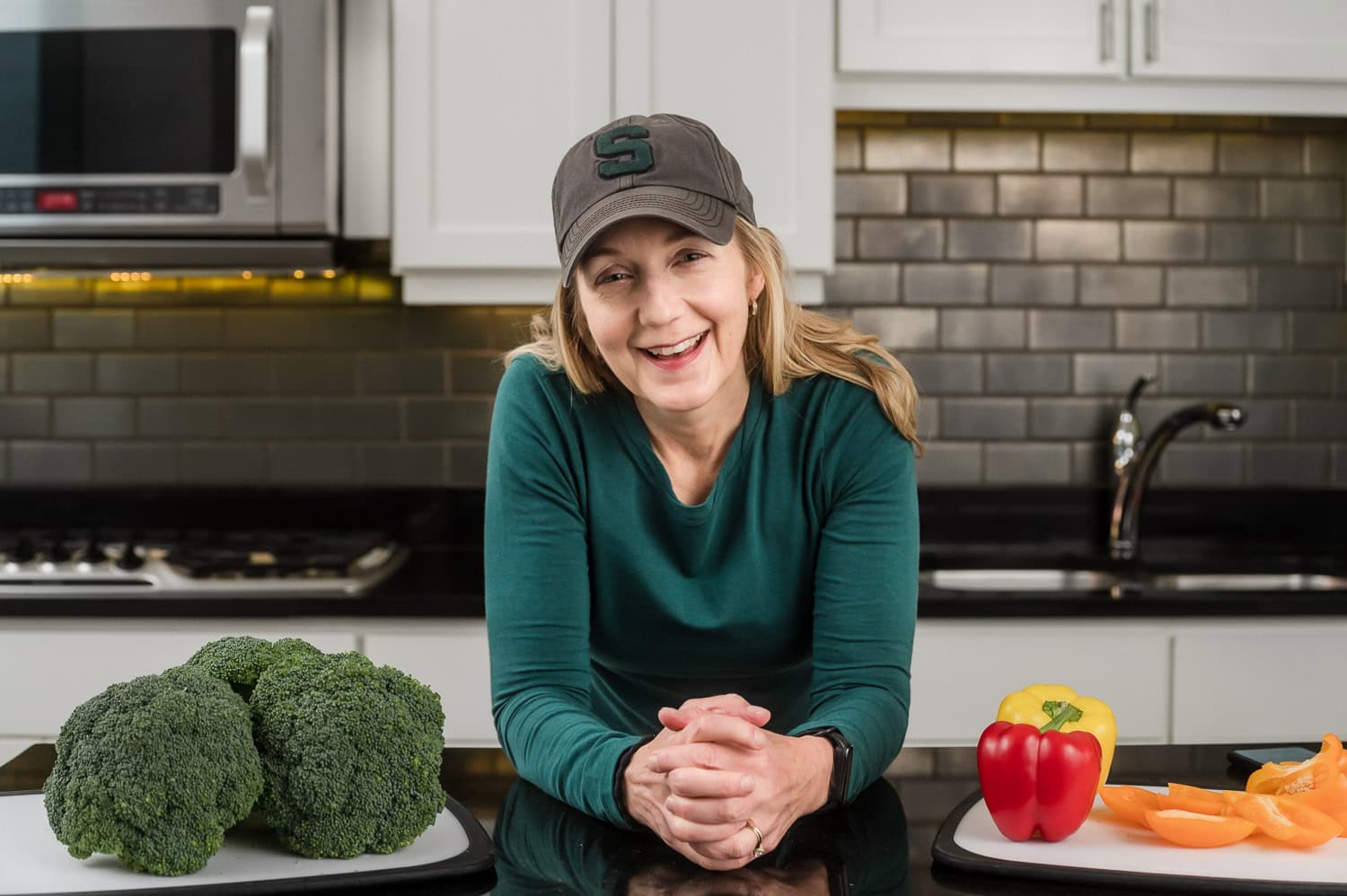 Female leans on counter with vegetables to each side during a branding photography session