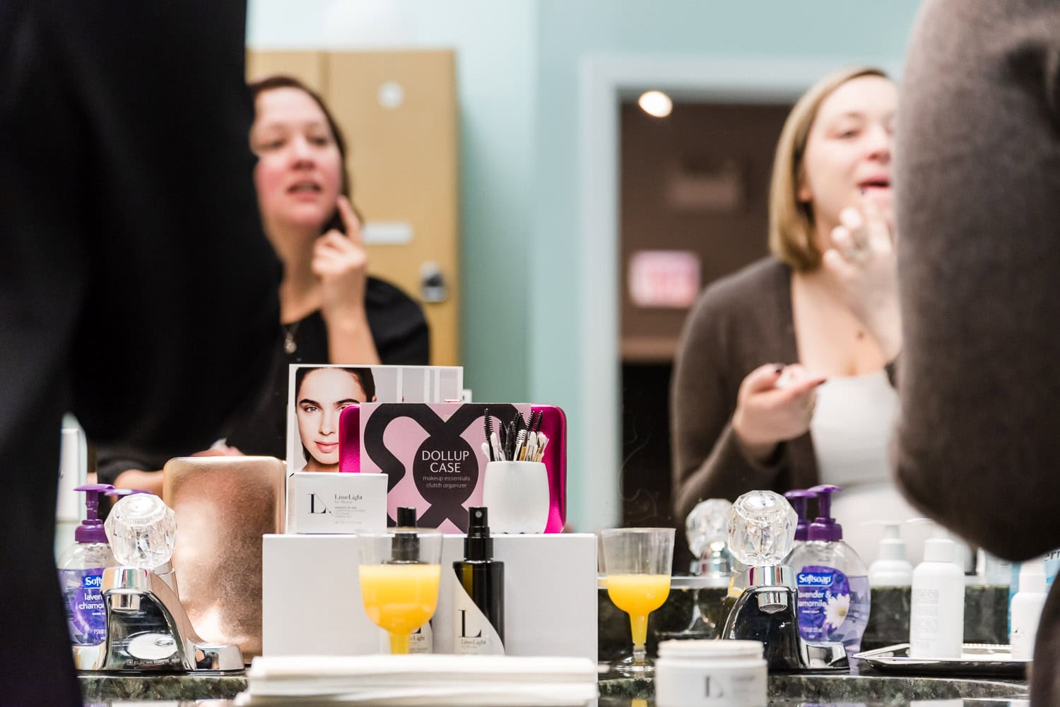 two women applying facial moisturizer while drinking mimosas in bathroom