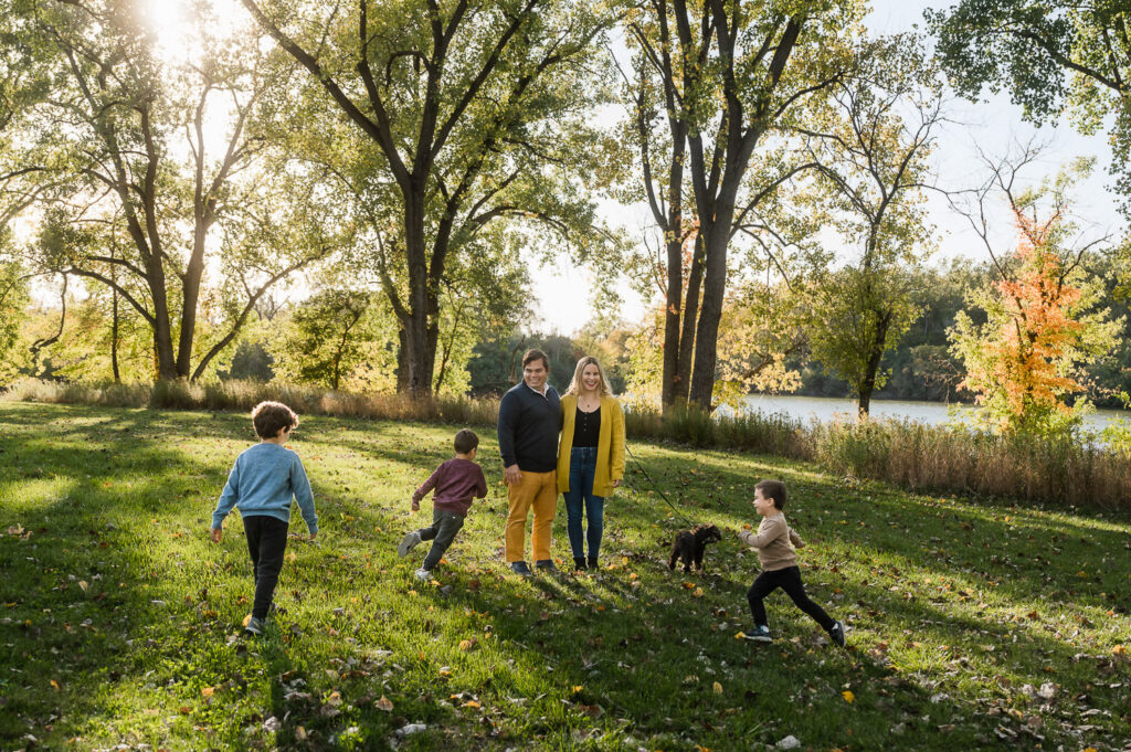 Mom and Dad hold dog while three sons run around them during a fall photo session at Skokie Lagoons