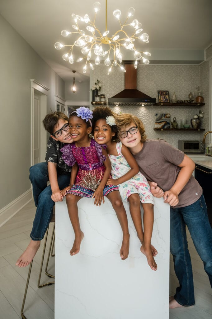 Mixed-race siblings squeeze together in a hug on their kitchen counter in their Lakeview home.