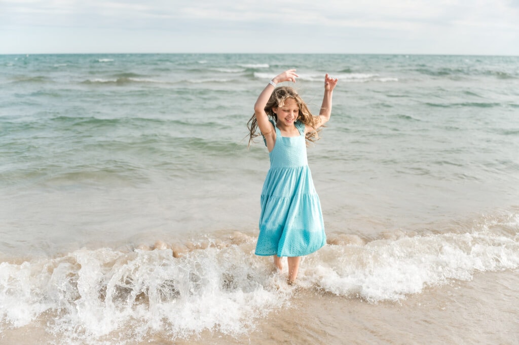 8 year old girl in teal dress dances ballet in the shores of Lake Michigan