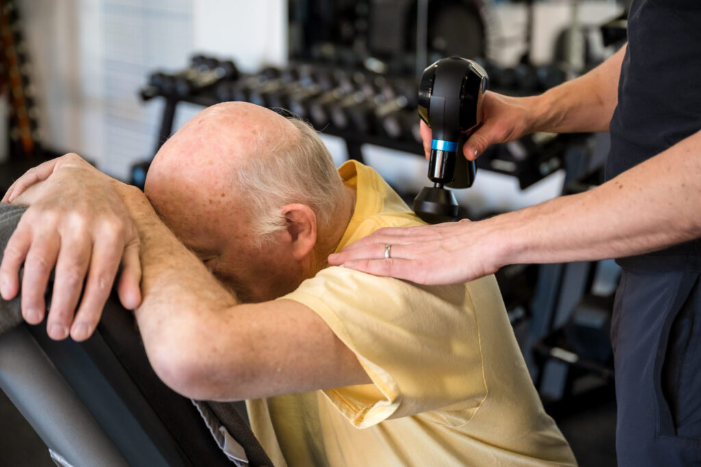 Detail of a theragun being used to give a client a shoulder massage after a workout