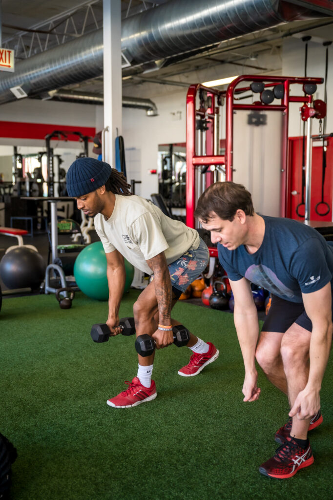 Personal trainer demonstrates weight lifting technique to a man during a gym workout