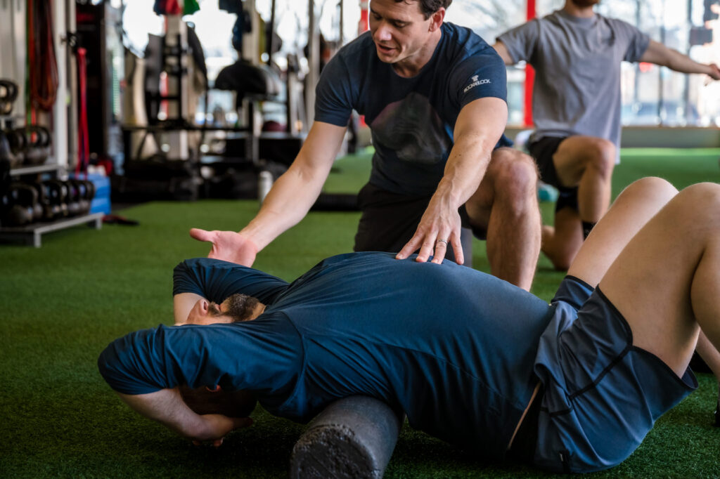 Personal trainer works with client who is stretching his back after a workout