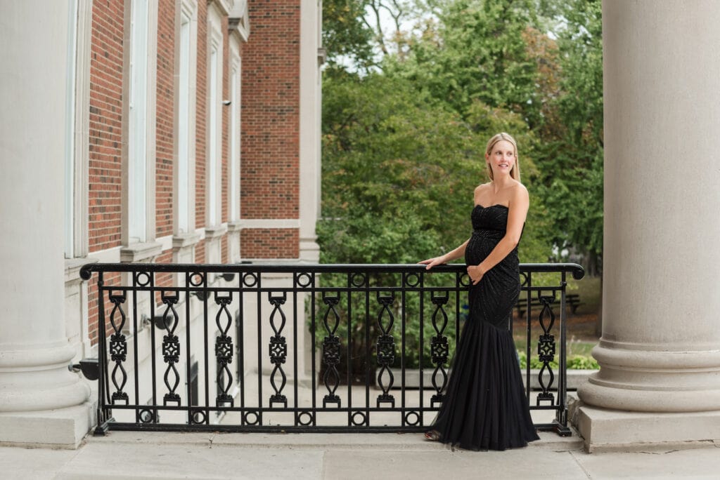 Woman who is pregnant and wearing an elegant long black dress holds railing at Chicago History Museum and looks over her shoulder to her partner off camera