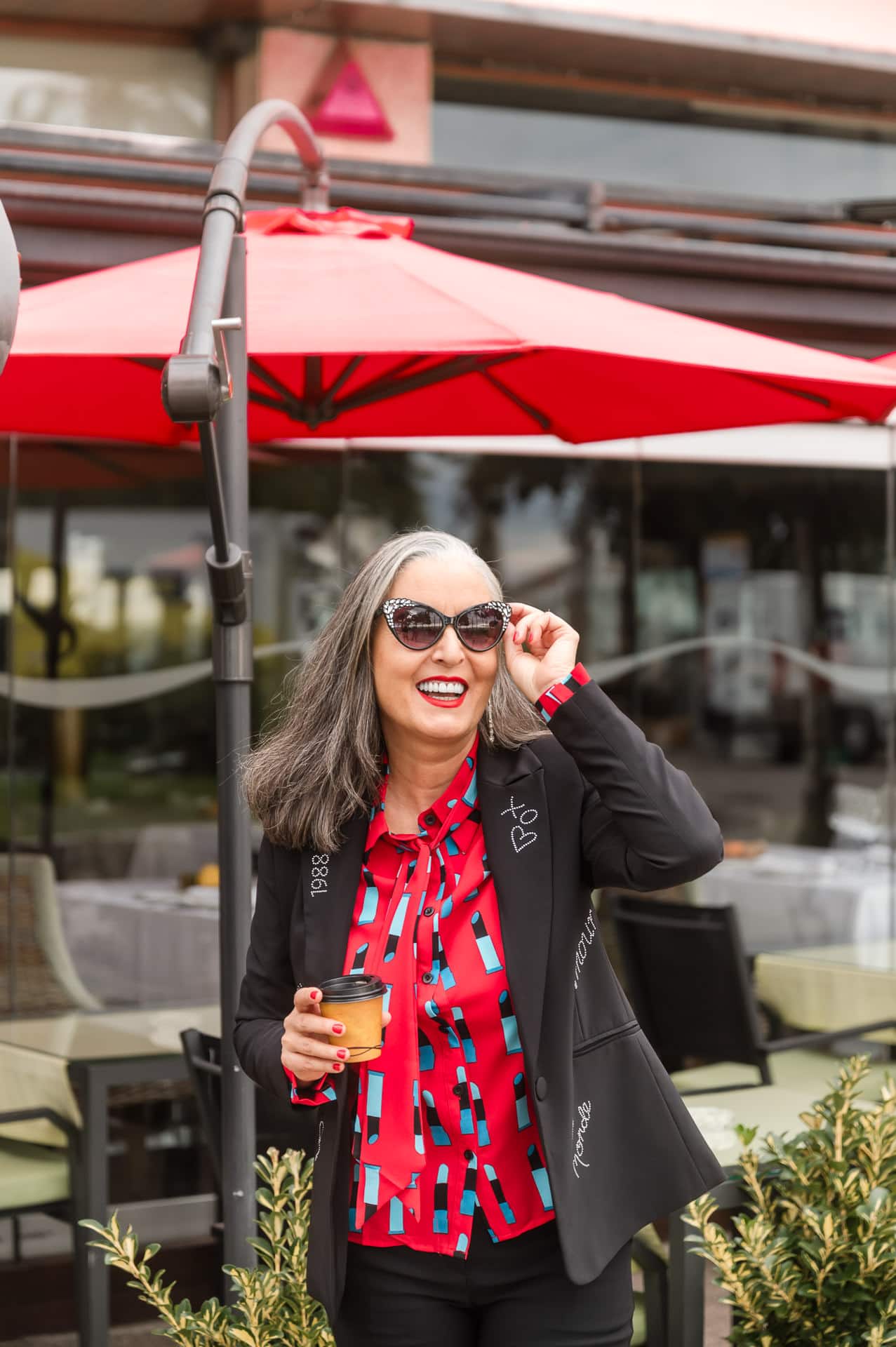 Woman adjusts her sunglasses with coffee in hand