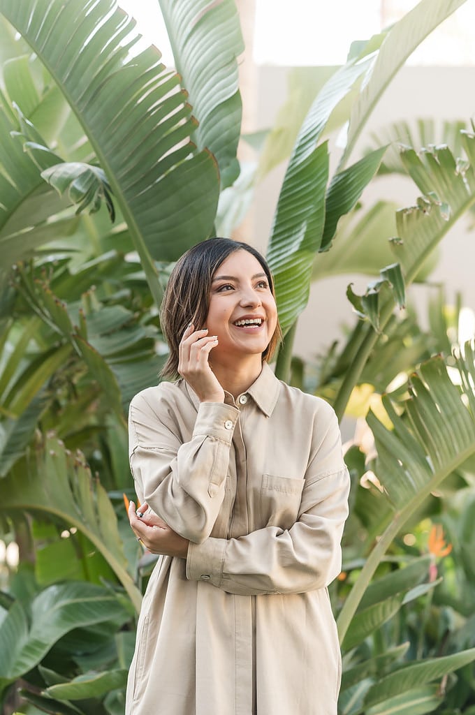 woman laughs up to the upper right of the frame with tropical plants behind her