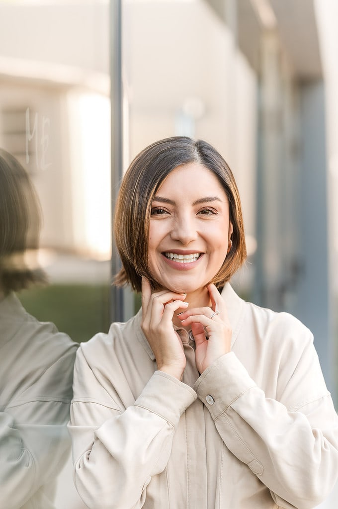 woman giggles with her hands framing her face with her reflection on the glass behind her