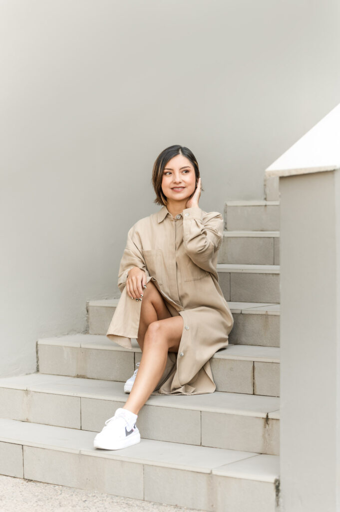 woman in khaki sits on gray stairway.