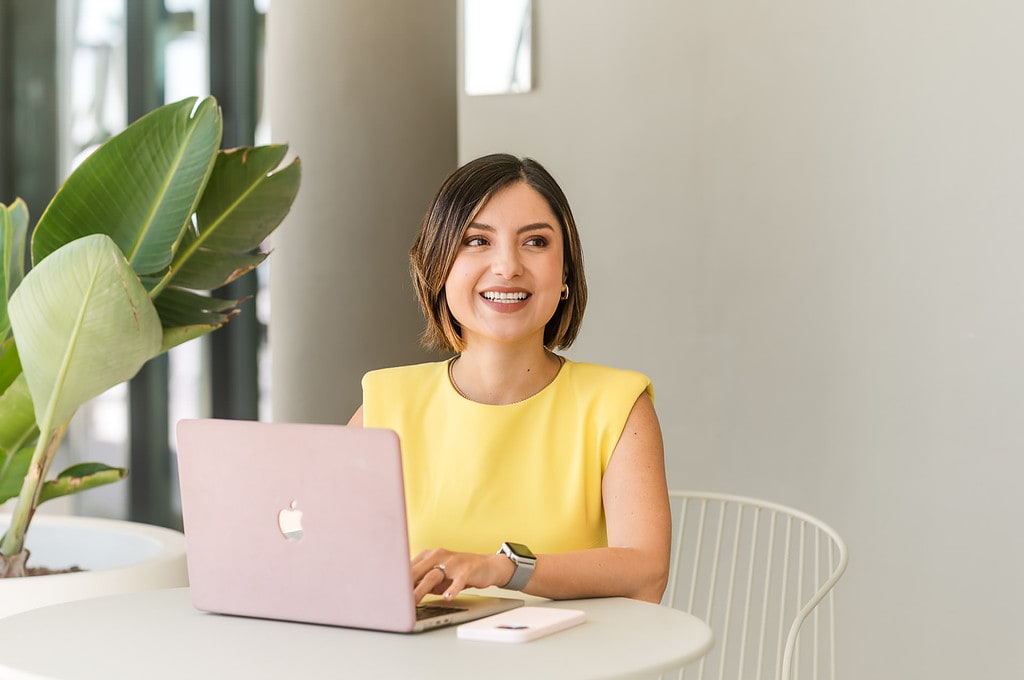 Woman wearing a yellow dress types at her yellow computer in a cafe