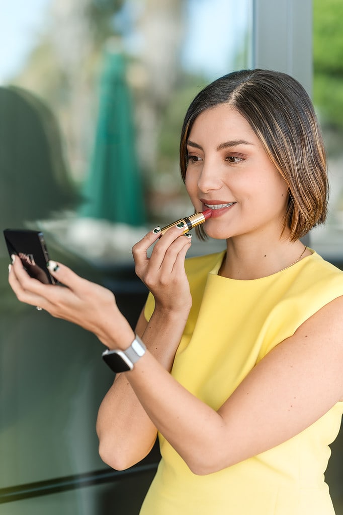 Woman wearing yellow puts on lipstick