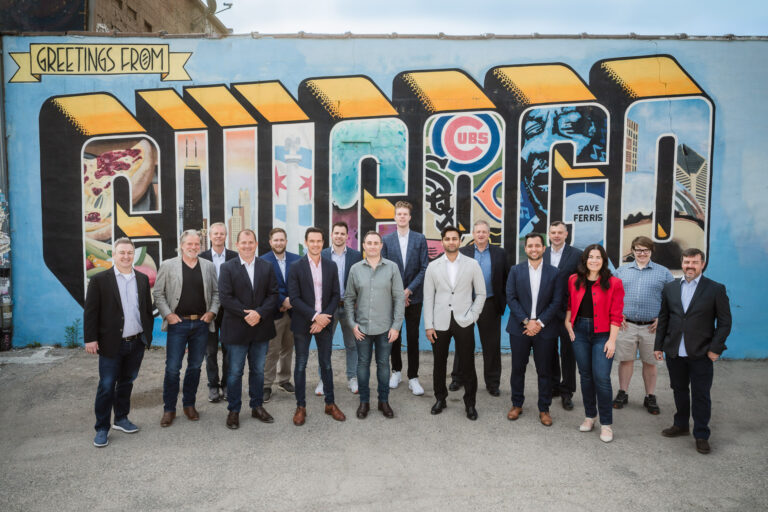 Group photo of Pomerol Partners team standing in front of the Greetings from Chicago mural
