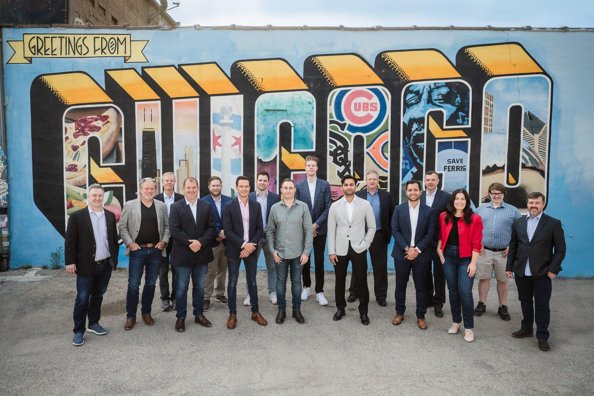 Group photo of Pomerol Partners team standing in front of the Greetings from Chicago mural