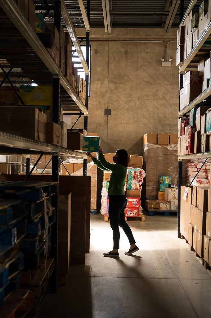 Silhouette of woman putting box of diapers onto shelf in a warehouse distribution center for families in need in Chicago