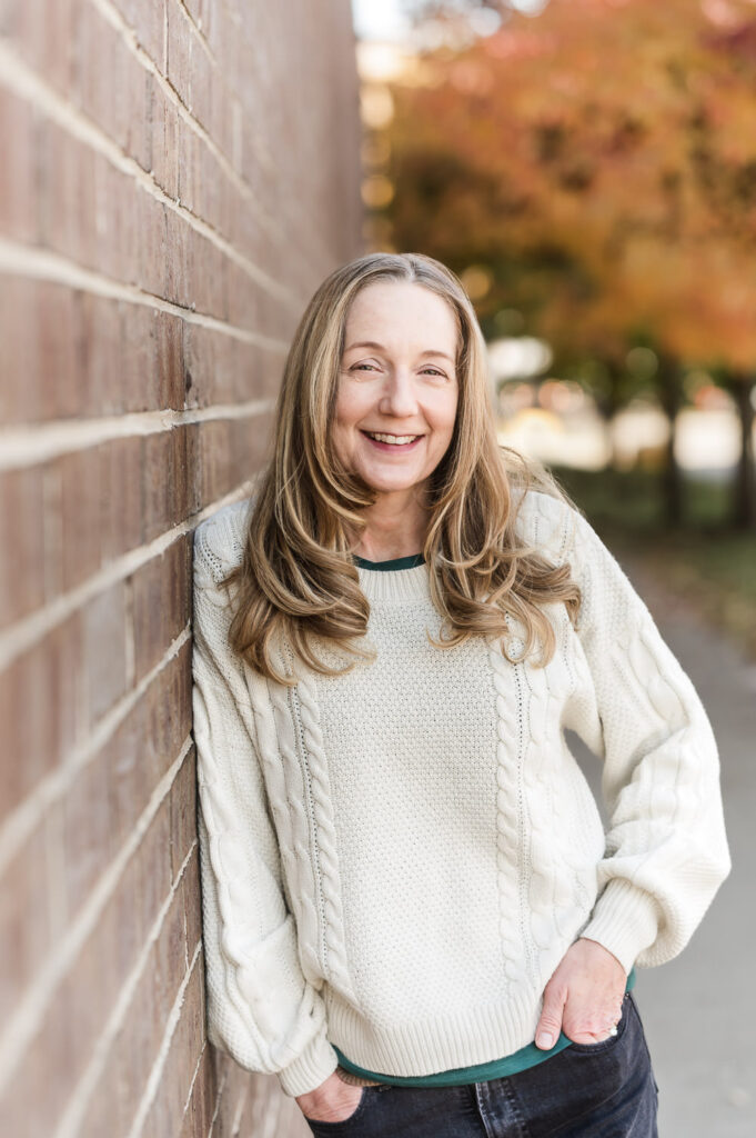 Woman leans against brick siding of building in Chicago with fall leaves in the backdrop