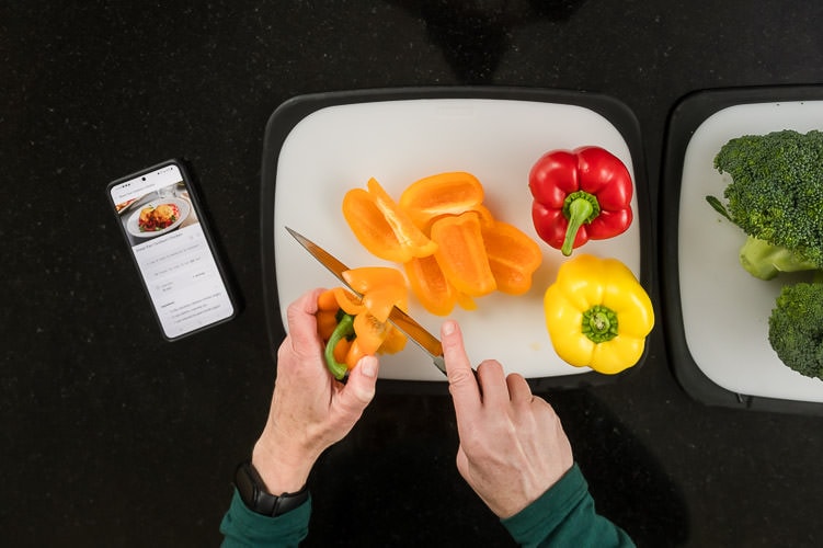 woman's hands cutting bell peppers while following a recipe on her iPhone