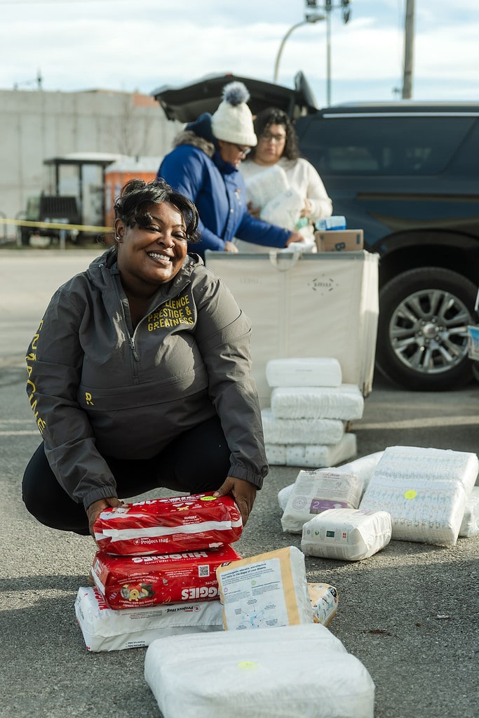 Woman kneels by diapers as she and other social workers sort them for their clients at a diaper distribution event