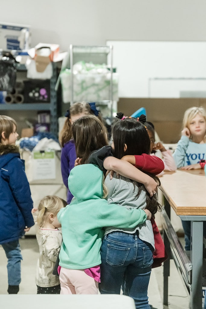 Volunteer kids hug at a sorting event for Share Our Spare