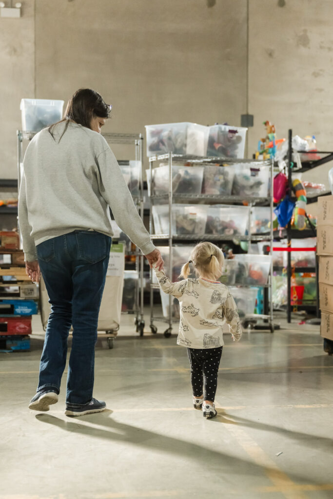 Caregiver and young girl walk through warehouse at Share Our Spare at a volunteer sorting event