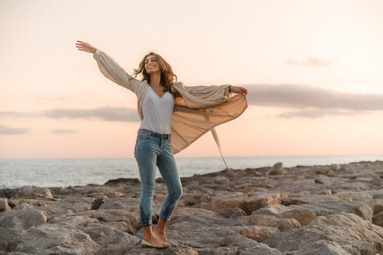 Woman throws her arms up in the air with a sunset backdrop of the beach in Chicago