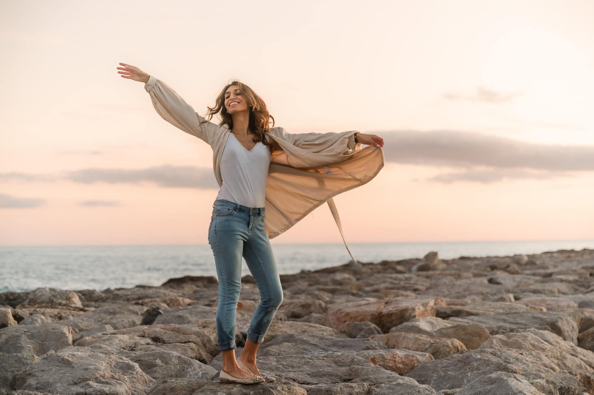 Woman throws her arms up in the air with a sunset backdrop of the beach in Chicago