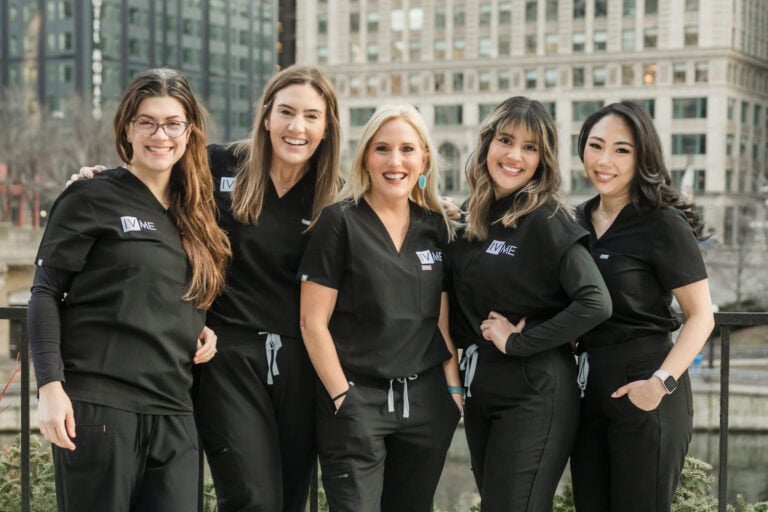 Group of 5 female nurse injectors wearing black scrubs stand in front of downtown Chicago background during a branding photo session for IVME River North