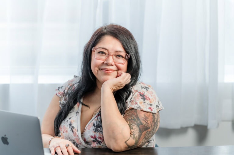 Woman with glasses leans in and smiles at the camera.