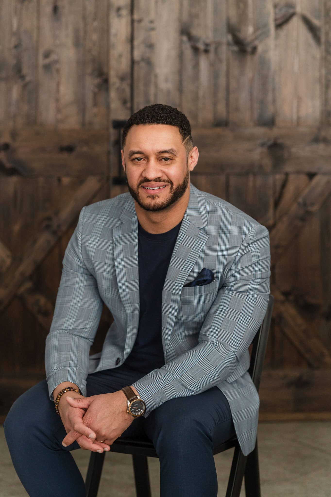 Man in navy blue blazer leans onto his knees in front of a dark wood door at a studio in Chicago