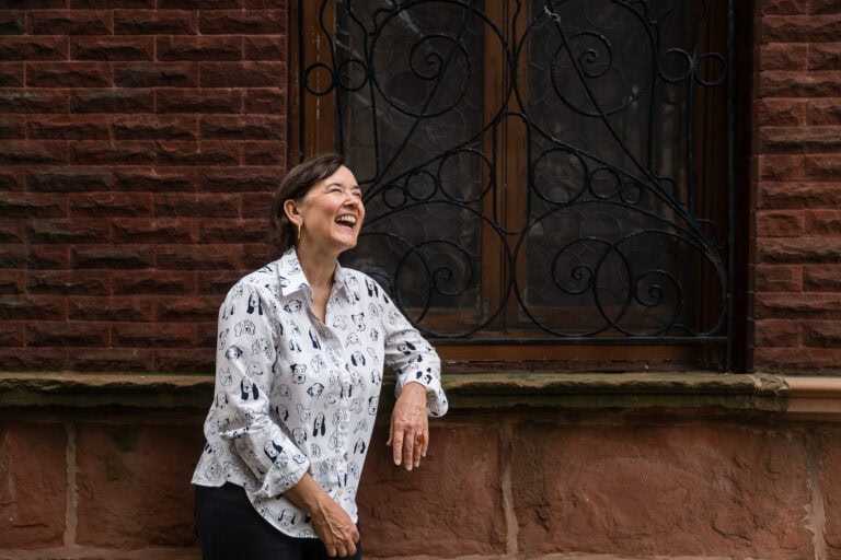Woman wearing a shirt covered in dogs leans on a window sill that has iron work texture surrounded by a red brick building in south loop Chicago