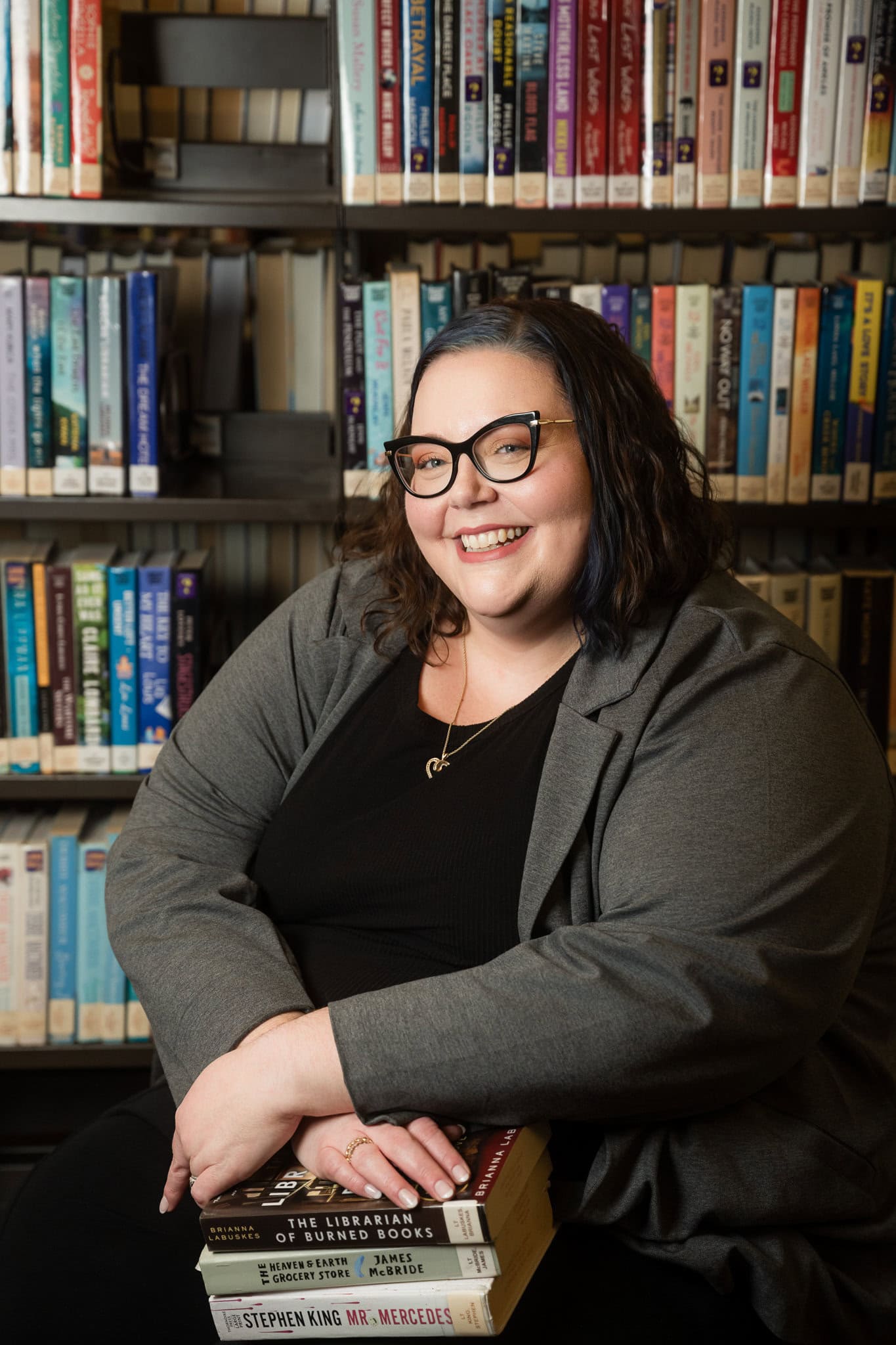 Jenn Jovanec Librarian in Dupage, a suburb of Chicago, sits in front on the fiction section with a pile of books she wants to read on her lap