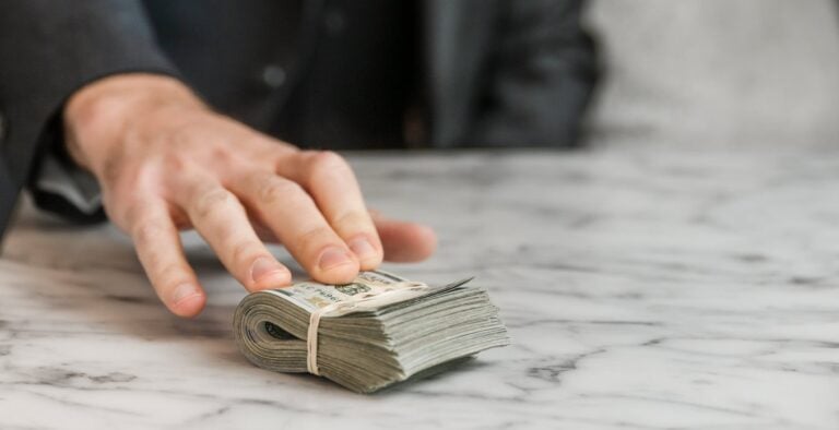 A detail of a hand on a large folded stack of money.