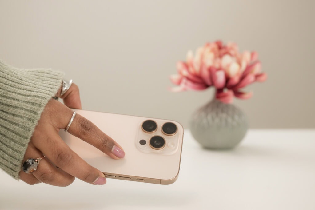 hand reaching for a pink iPhone with a pink flower on desk in background